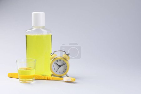 Foto de Enjuague bucal fresco en botella, vidrio, cepillo de dientes y despertador sobre fondo gris. Espacio para texto - Imagen libre de derechos
