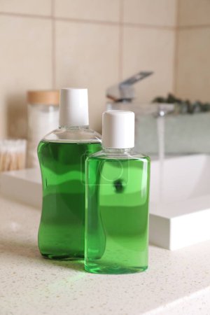 Fresh mouthwashes in bottles on countertop in bathroom, closeup