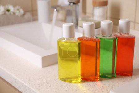 Fresh mouthwashes in bottles on countertop near sink, closeup. Space for text