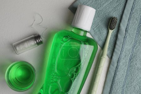 Foto de Enjuague bucal fresco en botella, vidrio, cepillo de dientes y hilo dental sobre fondo claro, puesta plana - Imagen libre de derechos