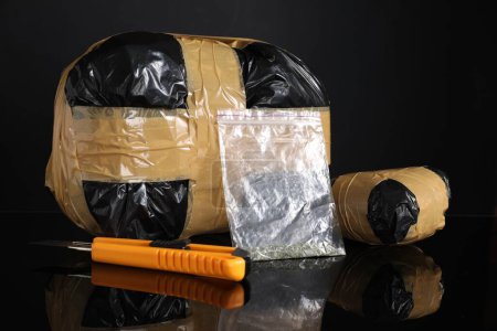 Schmuggel, Drogenhandel. Pakete mit Betäubungsmitteln und Gebrauchsmesser auf schwarzer Spiegeloberfläche