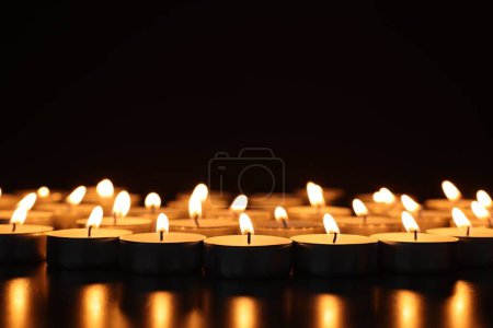 Brûler des bougies sur une surface sombre sur fond noir, gros plan. Espace pour le texte