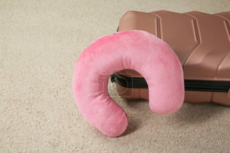 Pink travel pillow and suitcase on beige rug, space for text