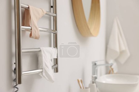 Beheizter Handtuchhalter mit Unterwäsche an weißer Wand im Badezimmer, Nahaufnahme