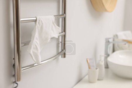 Beheizter Handtuchhalter mit Unterwäsche an weißer Wand im Badezimmer, Nahaufnahme