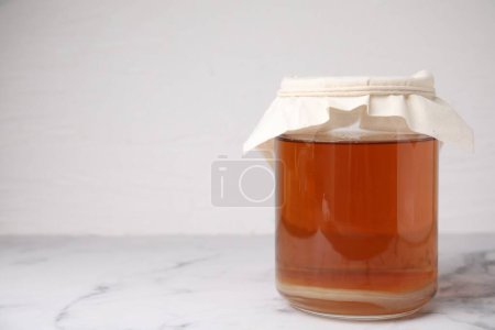Tasty kombucha in glass jar on white marble table, space for text