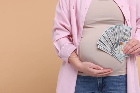 Téléchargez les photos : Mère porteuse. Femme enceinte avec des billets en dollars sur fond beige, gros plan. Espace pour le texte - en image libre de droit