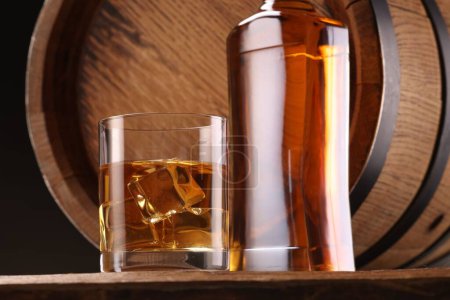 Whisky con cubitos de hielo en vidrio, botella y barril sobre mesa de madera