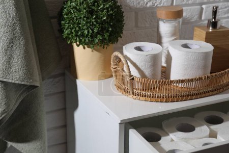 Toilet paper rolls, floral decor, dispenser and cotton pads on chest of drawers indoors