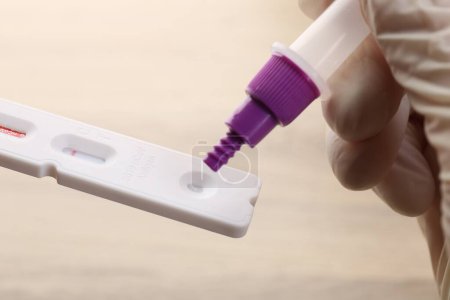 Doctor dropping buffer solution onto disposable express test cassette against blurred background, closeup