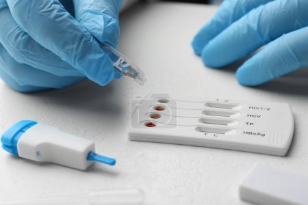 Arzt lässt Pufferlösung auf Einweg-Testkassette für Multiinfektionen an weißem Tisch fallen, Nahaufnahme