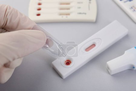 Doctor dropping buffer solution onto disposable express test cassette on light background, closeup