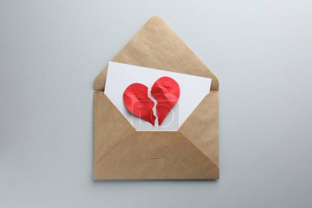 Enveloppe avec des moitiés de coeur en papier rouge déchiré sur fond blanc, vue de dessus. Coeur brisé
