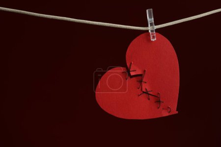 Coeur brisé. Coeur en papier rouge déchiré cousu avec fil sur corde sur fond bordeaux, espace pour le texte