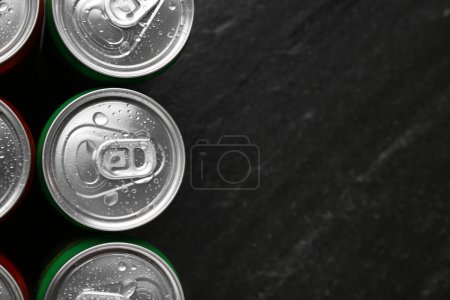 Energy drink in wet cans on black textured background, top view. Space for text