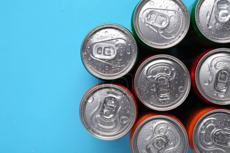 Energy drinks in wet cans on light blue background, top view. Space for text