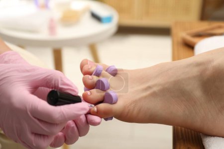 Pedicurista profesional pintando uñas de los pies del cliente con esmalte en salón de belleza, primer plano