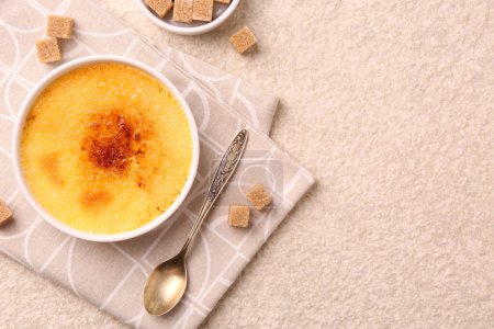 Photo for Delicious creme brulee in bowl, sugar cubes and spoon on light textured table, top view. Space for text - Royalty Free Image