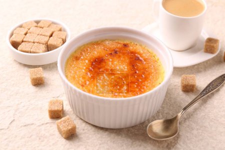 Delicious creme brulee in bowl, sugar cubes, coffee and spoon on light textured table, closeup