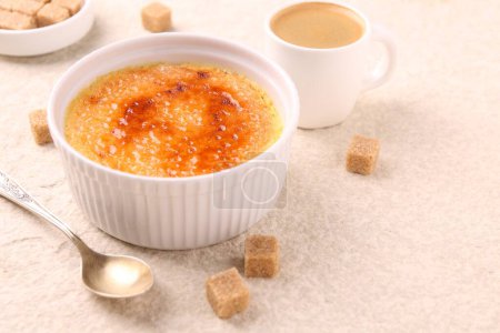 Foto de Deliciosa crema brulee en tazón, terrones de azúcar, café y cuchara en la mesa de textura ligera, primer plano. Espacio para texto - Imagen libre de derechos