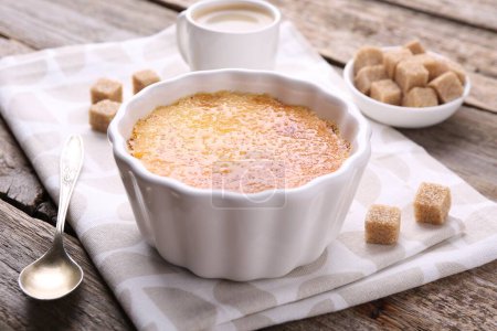 Foto de Deliciosa crema brulee en tazón, cubos de azúcar y cuchara en la mesa de madera, primer plano - Imagen libre de derechos