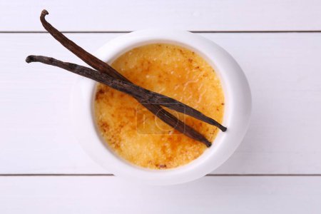 Foto de Deliciosa crema brulee en tazón y vainas de vainilla en mesa de madera blanca, vista superior - Imagen libre de derechos