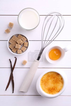 Photo for Delicious creme brulee in bowl and ingredients on white wooden table, flat lay - Royalty Free Image
