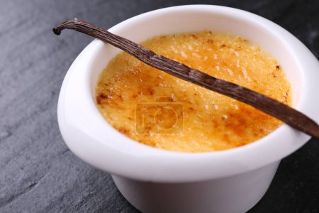 Photo for Delicious creme brulee in bowl and vanilla pod on dark gray textured table - Royalty Free Image