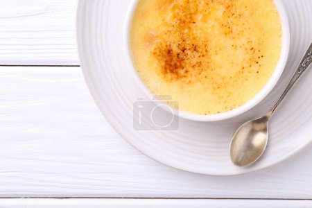 Téléchargez les photos : Délicieuse crème brulée dans un bol et cuillère sur table en bois blanc, vue sur le dessus - en image libre de droit