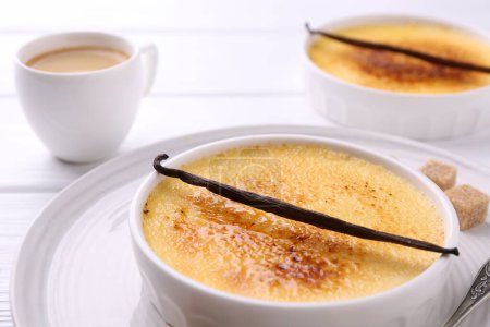 Téléchargez les photos : Délicieuse crème brulée dans des bols, gousses de vanille, cubes de sucre et café sur table en bois blanc, gros plan - en image libre de droit