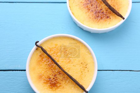 Téléchargez les photos : Délicieuse crème brulée dans des bols et des gousses de vanille sur table en bois bleu clair, vue sur le dessus - en image libre de droit