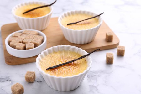 Téléchargez les photos : Délicieuse crème brulée dans des bols, gousses de vanille et cubes de sucre sur table en marbre blanc, gros plan - en image libre de droit