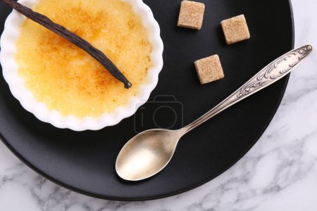 Téléchargez les photos : Délicieuse crème brulée dans un bol, gousse de vanille, cubes de sucre et cuillère sur table en marbre blanc, vue sur le dessus - en image libre de droit