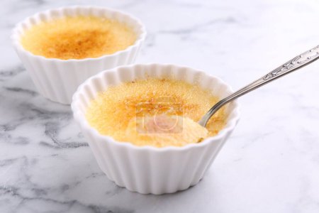 Téléchargez les photos : Délicieuse crème brulée dans des bols et cuillère sur table en marbre blanc, gros plan - en image libre de droit