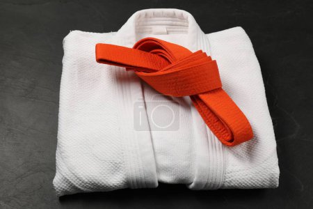 Cinturón de karate naranja y kimono blanco sobre fondo gris