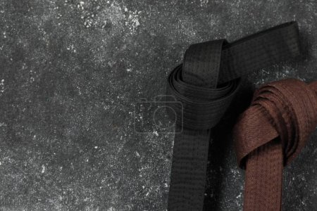 Cinturones de karate negros y marrones sobre fondo texturizado gris, planas. Espacio para texto