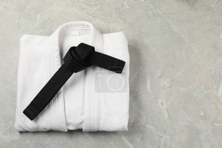 Black karate belt and white kimono on gray marble background, top view. Space for text