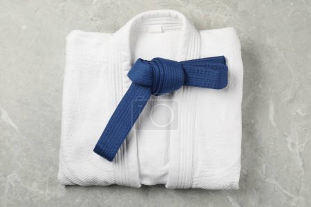 Cinturón de karate azul y kimono blanco sobre fondo de mármol gris, vista superior