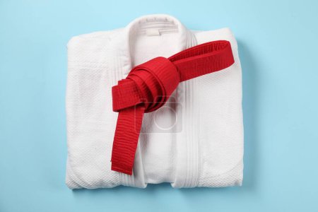 Red karate belt and white kimono on light blue background, top view