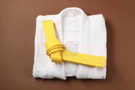 Cinturón de karate amarillo y kimono blanco sobre fondo marrón, vista superior