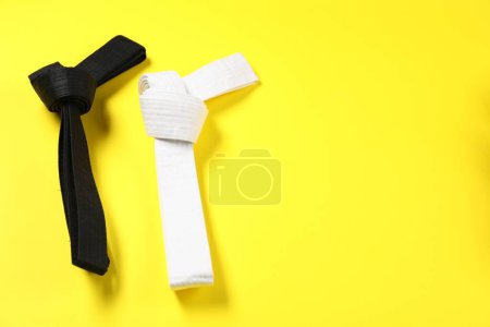 Photo for Black and white karate belts on yellow background, flat lay. Space for text - Royalty Free Image