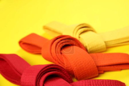 Colorful karate belts on yellow background, closeup