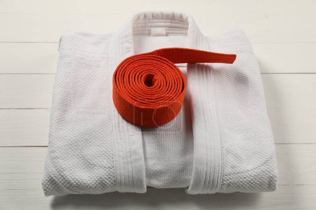 Cinturón de karate naranja y kimono blanco sobre fondo de madera