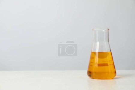 Glass flask with yellow oil on white table, space for text