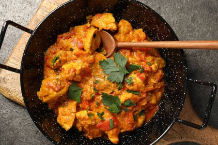Delicioso curry de pollo en sartén y cuchara sobre mesa gris, vista superior