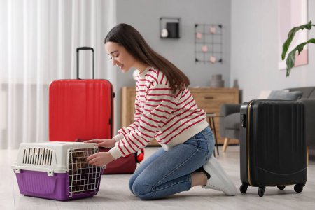 Lächelnde Frau bereitet sich darauf vor, mit Hund im Haus zu reisen. Koffer und Haustierhalter um sie herum
