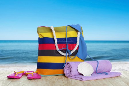Stilvolle gestreifte Tasche und andere Strandaccessoires auf Holztisch am Meer