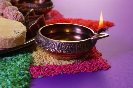 Téléchargez les photos : Fête de Diwali. Savoureux bonbons indiens, lampe diya et rangoli coloré sur table violette, gros plan - en image libre de droit