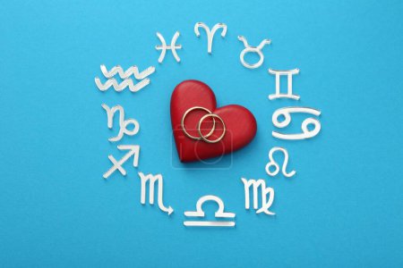 Foto de Signos del zodíaco, corazón y anillos de boda sobre fondo azul claro, posición plana - Imagen libre de derechos
