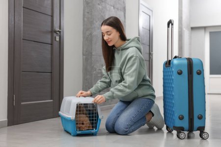 Travelling with pet. Woman looking at carrier with her dog in hall